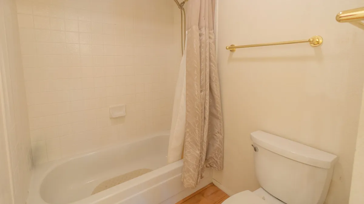 A simple and serene bathroom with a bathtub, toilet, shower curtain, and golden towel rack. The space exudes calm, ideal for relaxing baths or morning routines with family.