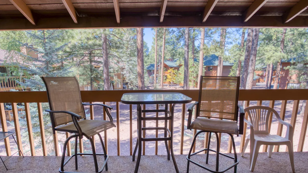 An exterior view from a private balcony with comfortable outdoor seating and a table, overlooking a tranquil forest landscape. The setting is calm and serene, perfect for sipping coffee, watching wildlife, or simply breathing in fresh mountain air.