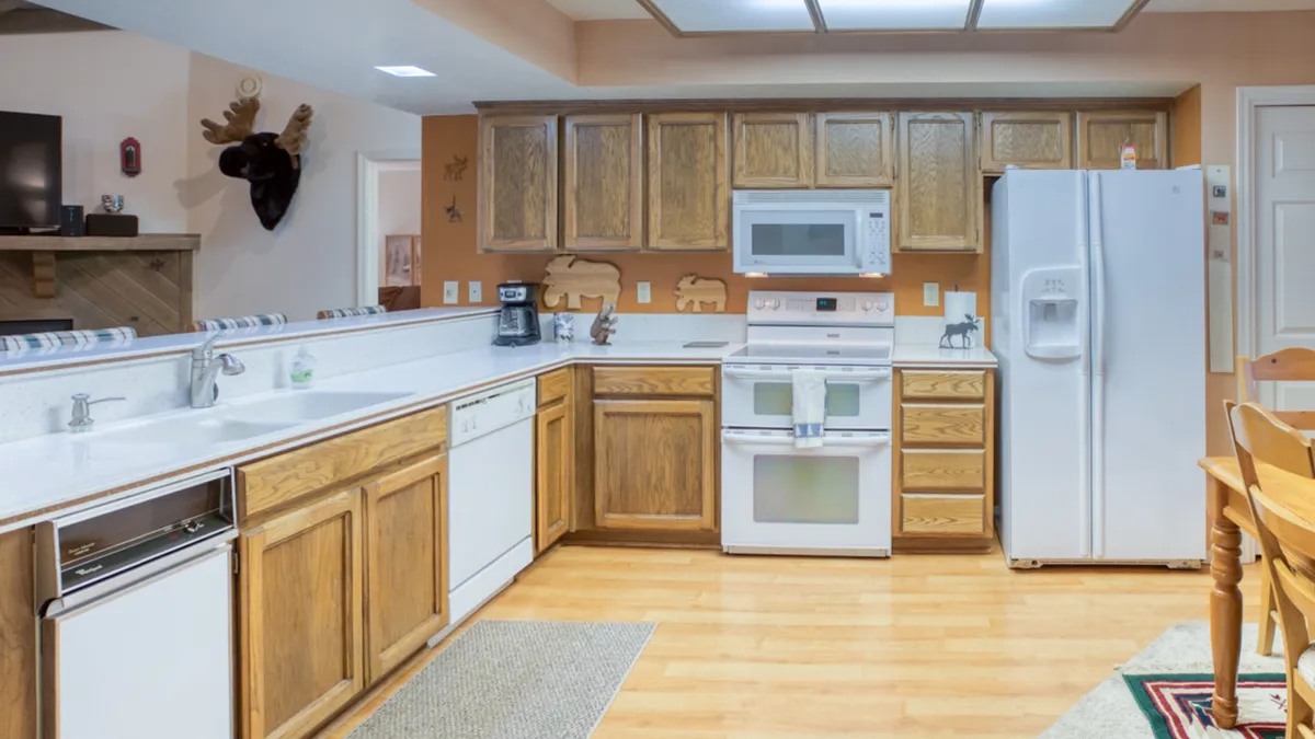 This image captures a welcoming kitchen scene featuring a central kitchen island, warm wooden cabinetry, and modern appliances prominently in view. The atmosphere suggests a space designed for both culinary creativity and social gatherings, with ample workspace and storage.