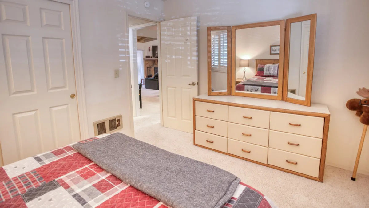 A cozy bedroom featuring a dressing table with mirrors, a bed adorned with patterned bedding, and a soft gray blanket. Natural light filters in, suggesting a space that blends comfort and a sense of retreat after a day of outdoor adventures.