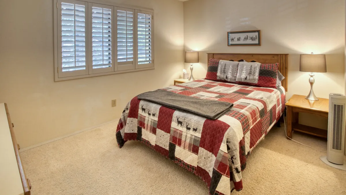A welcoming bedroom with a patterned quilt on the bed, nightstands with warm lamps, and shuttered windows that let in morning light. The inviting atmosphere suggests relaxation and quiet moments spent together.