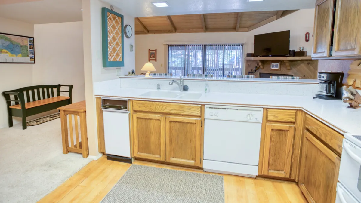 A bright kitchen setting with a kitchen counter, wooden cabinets, built-in dishwasher, a bench for seating, and a window that bathes the space in natural light. It showcases practical workspace and an inviting atmosphere for both cooking and casual dining.